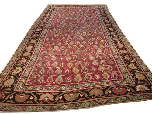 6x14 antique Persian Kerman gallery rug angled view showing red paisley field and dark floral border