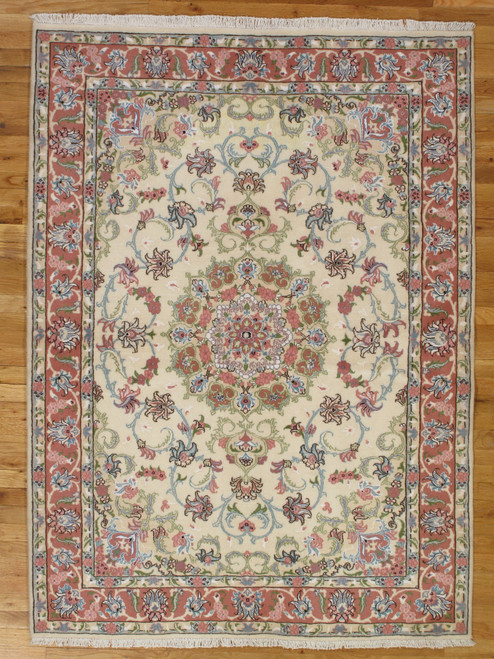 Ivory field Persian Tabriz rug with coral floral border and central rosette medallion on wood floor