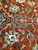 Detail of a brown and sage cartouche with ivory tendrils on soft rust coral wool