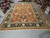 Warehouse floor photograph of the oversize rust and navy rug beside stacked rolled Oriental rugs