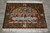 Whole rug laid flat on grey tile, fringes at top and bottom, seen straight on