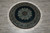 Overhead view of the round rug lying on a grey tiled floor with fringe fanned out evenly