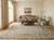 Rug in a cream sitting room beneath a camelback sofa, coffee table and two green armchairs