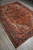 Full rug photographed from one end on grey plank flooring, ivory spandrels against red field