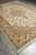 Diagonal floor view showing beige main border, sage guard stripes and ivory cotton fringe ends