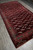 Long diagonal view showing burgundy field, ivory diamond guls and cream fringe on tribal wool rug