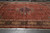 Rust red Tabriz rug photographed lengthwise in the warehouse showing navy medallion and green cartouche border
