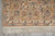 Corner detail of the tan border, ivory guard stripes and hand-tied fringe on grey floor