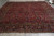 Burgundy Sarouk area rug laid flat on grey warehouse floor showing all over floral sprays