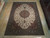 9x12 Persian Tabriz rug photographed on hardwood showroom floor beside other hand-knotted Oriental rugs