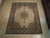 Ivory and sage wool and silk Tabriz rug displayed flat on light wood flooring