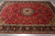 Berry red wool and silk Tabriz rug angled on grey tile floor showing dense floral field