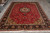 Large 8x12 Persian rug photographed in the warehouse showroom with rolled inventory stacked behind