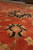 Black and gold palmette medallion detail set against the deep rust red wool field