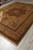 Angled view of large wool area rug showing champagne field, floral spandrels and triple borders