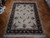 Ivory hand-knotted rug displayed on herringbone parquet floor showing black border and floral field