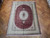 Burgundy and ivory pure silk Qum rug displayed flat on herringbone parquet wood floor