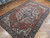 7x11 antique Heriz Serapi rug angled on parquet, ivory corner spandrels and indigo border visible