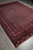 Vintage 1970s Oriental rug photographed lengthwise, red borders and ivory fringe against grey tile floor