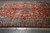 Red field oversize Persian rug shot at an angle showing dense floral vinework and slate blue border