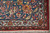 Corner close-up of blue border with red flowers, ivory guard stripe and clean cotton fringe