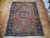 Rust and indigo Persian village rug displayed flat on herringbone parquet floor in showroom