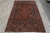 4x7 antique Persian rug seen lengthwise on grey stone tile, navy field and red border