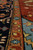 Detail of camel gold guard border beside indigo main border, angled low-light weave view