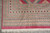 Corner of the 9' x 13' wool rug with cream fringe and repeating diamond border bands
