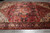 Angled view showing brick red field, olive gold outer border and dense hand-knotted wool pile