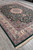 9'4" x 13' green area rug angled on grey tile, ivory border and cream fringe visible
