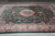 9x13 green Tabriz design rug seen lengthwise with ivory floral border on concrete