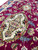 Ivory lozenge medallion outlined in gold with coral rosettes, photographed at an angle across pile