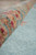 Close-up of rolled pile edge highlighting plush wool depth, salmon, crimson and pale green floral tones