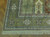 Corner detail showing olive green main border, rosette medallions, multiple guard stripes and ivory fringe