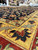 Saffron border detail photographed in the rug warehouse, showing sage green leaves and red blossoms
