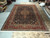 13'2 x 19'9 Persian Tabriz rug displayed flat on showroom floor beside stacked rolled rugs