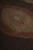 Overhead detail of concentric medallion tiers blending rust, gold and olive over a dark ground