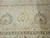 Close-up of wheat and sage palmette border framing the cream ivory field of this rug