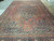 Angled view of oversize antique Tabriz rug showing brick field, navy corners and wide border