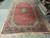10'8" x 20' Persian Kashan rug displayed full length on warehouse floor beside stacked rugs