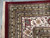 Corner detail of burgundy selvage, ivory floral border and thick wool pile with fringe