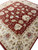 Hand-knotted wool rug photographed on the floor, ivory border blossoms meeting the brick red flowering field