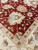 Corner detail where the terracotta field meets the ivory border, serrated leaves and garnet rosettes
