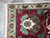 Corner detail of cream guard border, burgundy palmette and hand-tied ivory fringe on wool rug
