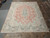 10' x 12'10" Persian Kerman rug shown flat on stone showroom floor beside rolled rugs