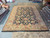 Oversize 12x18 hand-knotted wool rug displayed flat on showroom floor beside rolled Oriental rugs