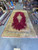 12 x 22 palace size Kerman rug displayed flat on warehouse floor among rolled Persian rugs