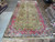8'9" x 18'8" Persian Kerman rug laid lengthwise on showroom floor beside rolled rugs