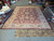 Full warehouse view of the hand-knotted burgundy Ziegler rug laid flat among rolled Oriental rugs